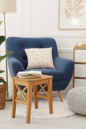 Photo of Stool, books, armchair and houseplant in room. Interior design