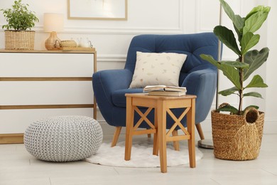 Photo of Stool, books, armchair and houseplants in room. Interior design