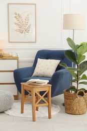 Photo of Stool, books, armchair and houseplant in room. Interior design