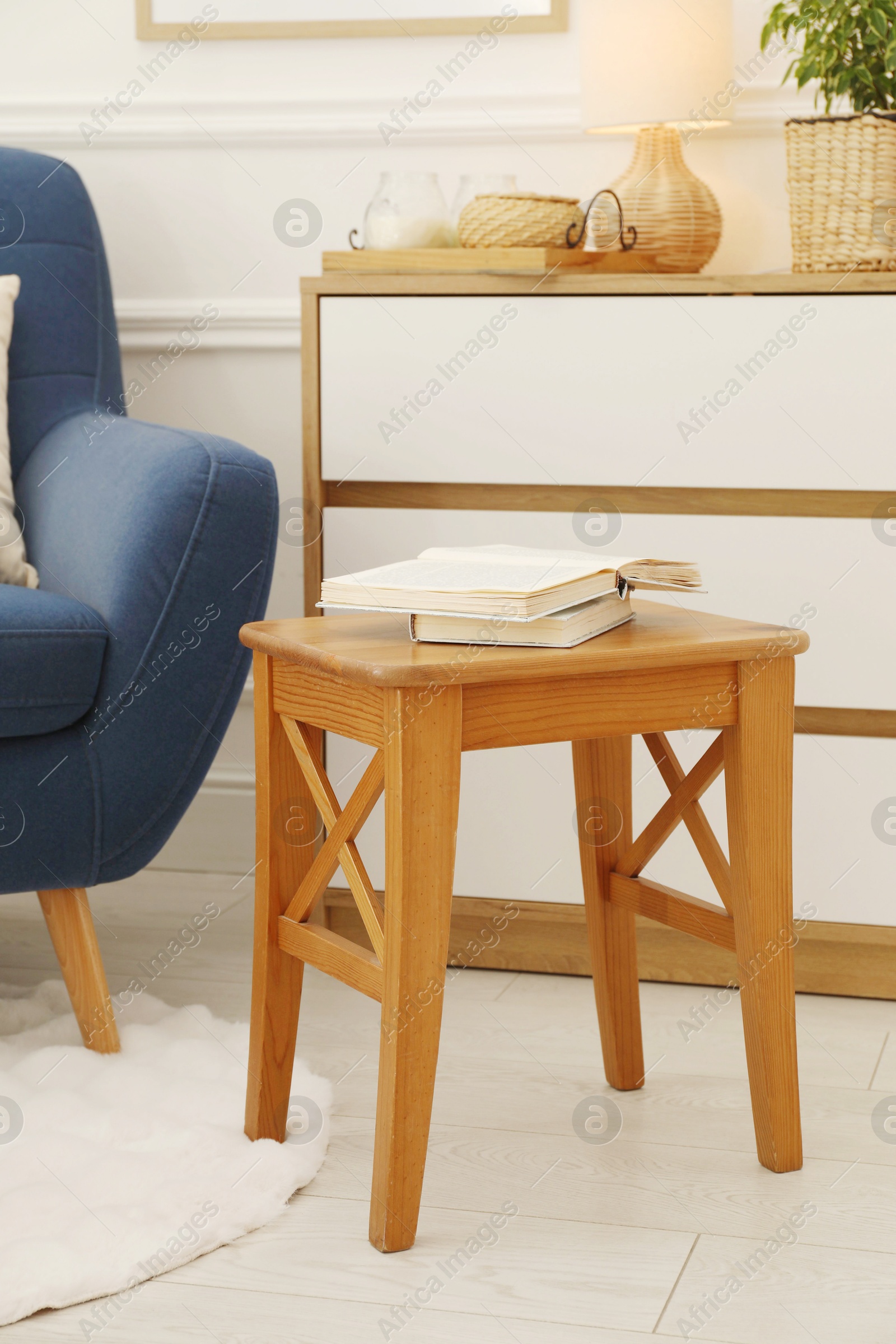 Photo of Stool, books, armchair and houseplant in room. Interior design