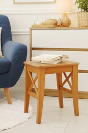 Photo of Stool, books, armchair and houseplant in room. Interior design