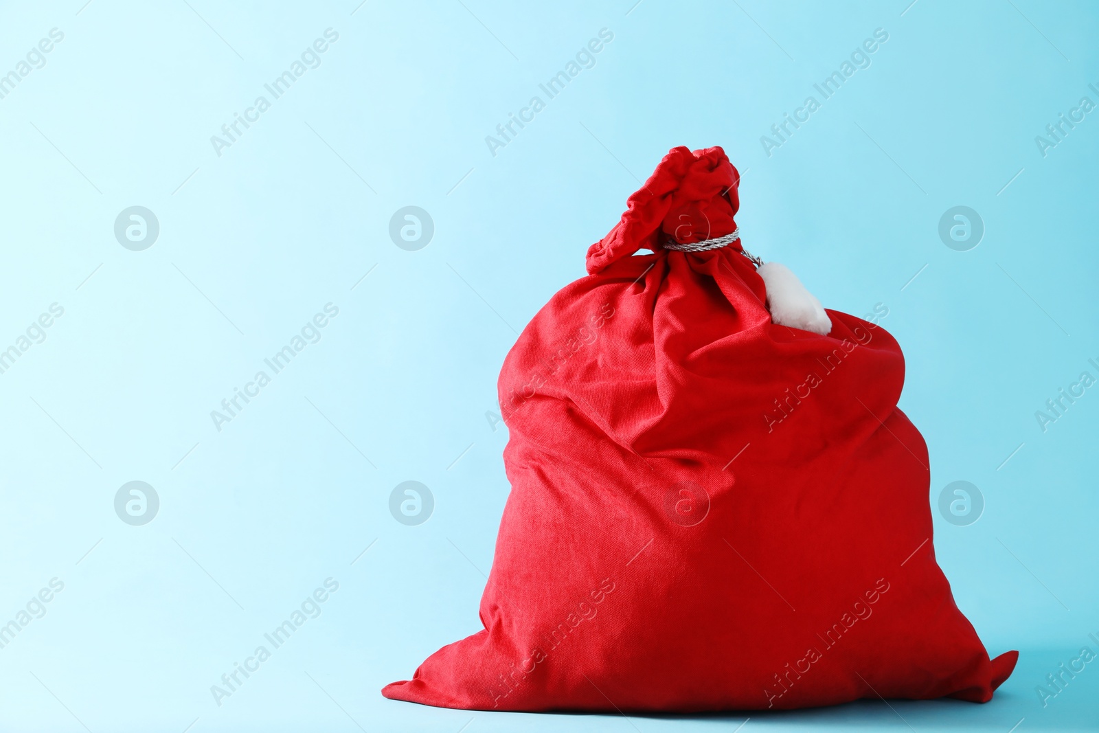 Red Santa Claus bag on light blue background, space for text Photo of Red Santa Claus bag on light blue background, space for text
