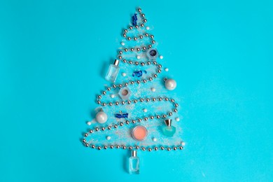 Photo of Christmas tree made of perfume bottles and makeup products on light blue background, flat lay