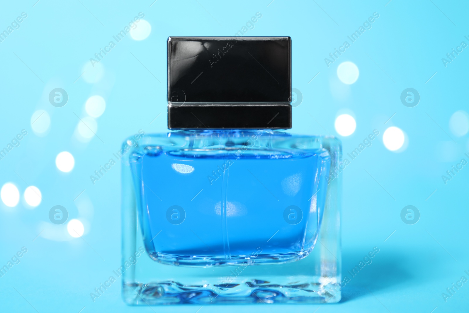 Photo of Perfume bottle on light blue background with blurred lights, closeup