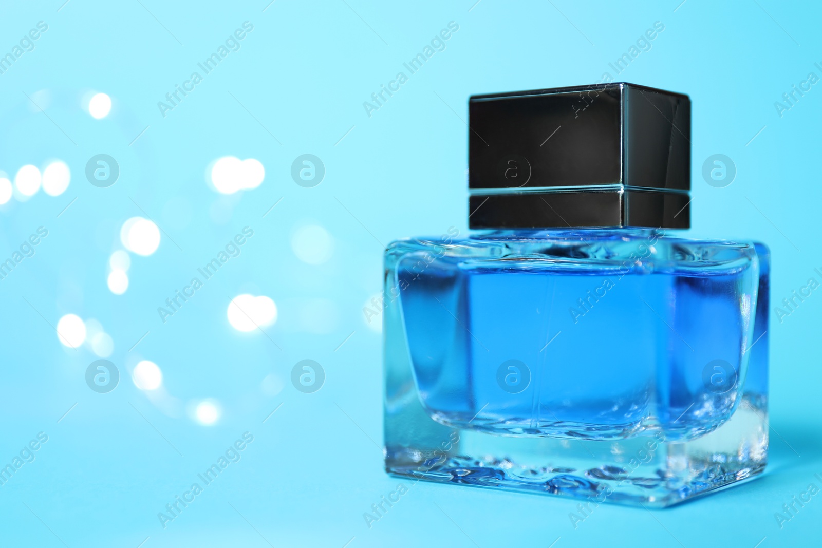 Photo of Perfume bottle on light blue background with blurred lights, closeup. Space for text