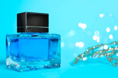 Photo of Perfume bottle on light blue background with blurred lights, closeup. Space for text