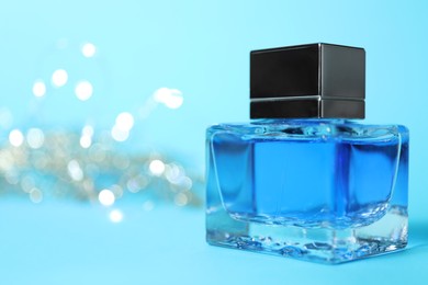 Photo of Perfume bottle on light blue background with blurred lights, closeup. Space for text