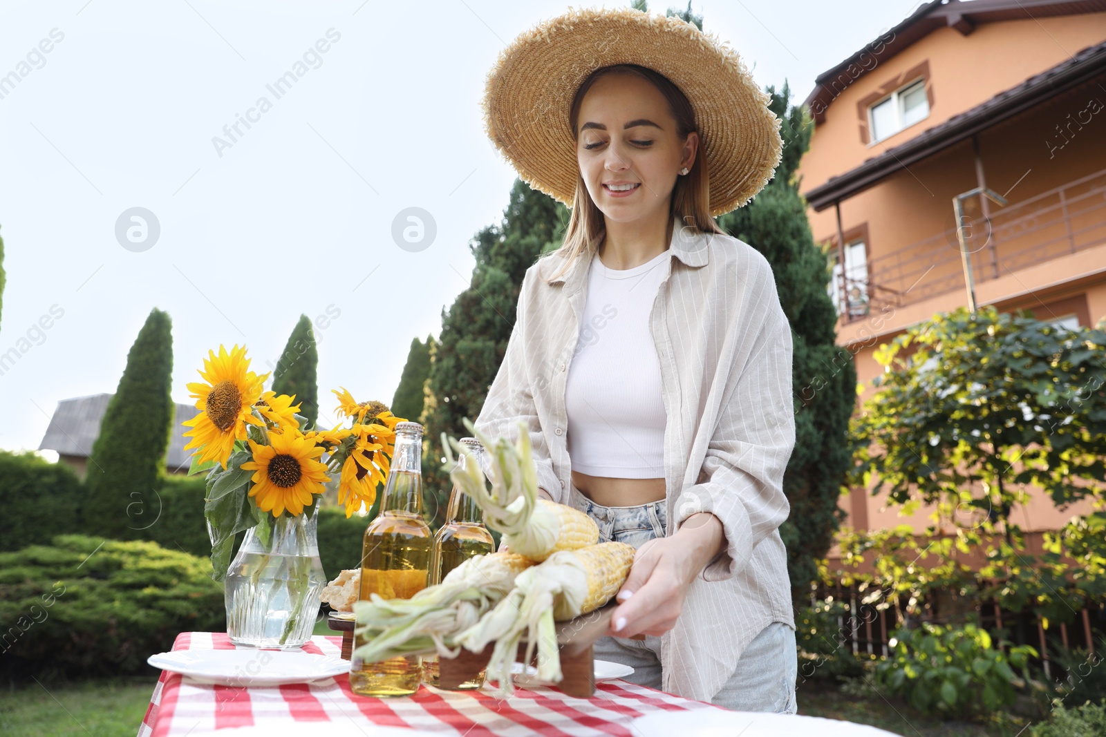 Photo of Beautiful woman with fresh corncobs near table in garden