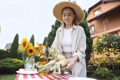 Beautiful woman with fresh corncobs near table in garden