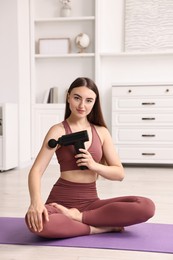 Woman using percussive massager to relieve arm muscles on mat at home