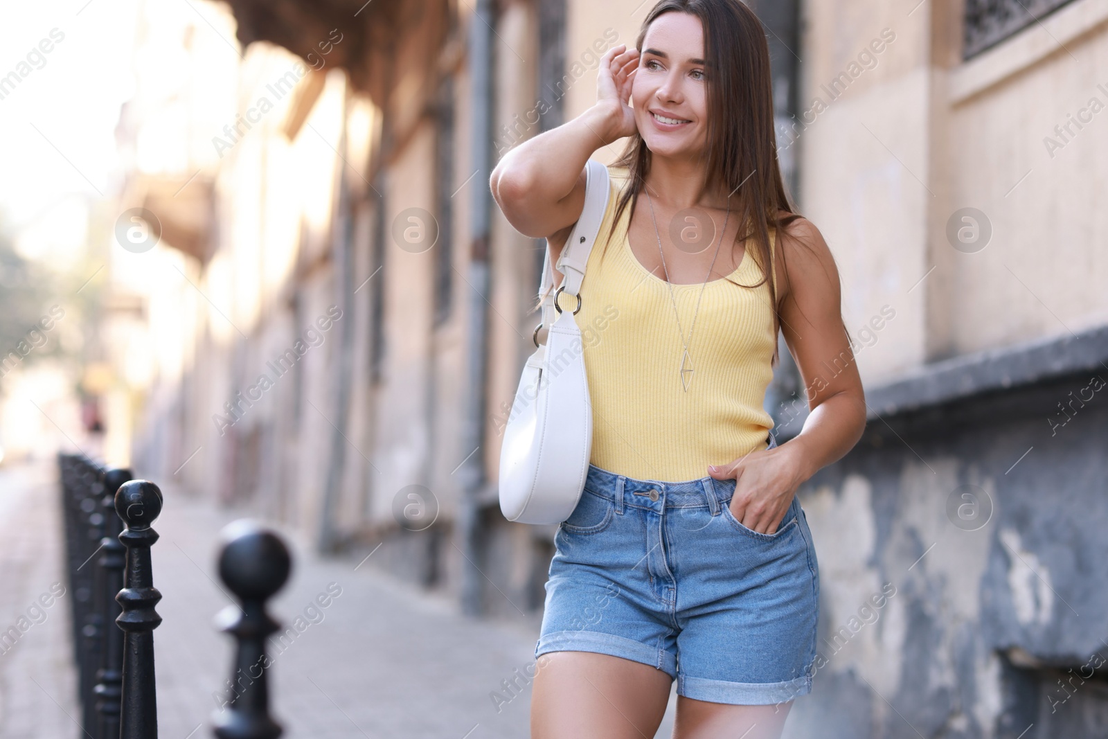 Photo of Beautiful woman with white bag wearing stylish denim shorts outdoors