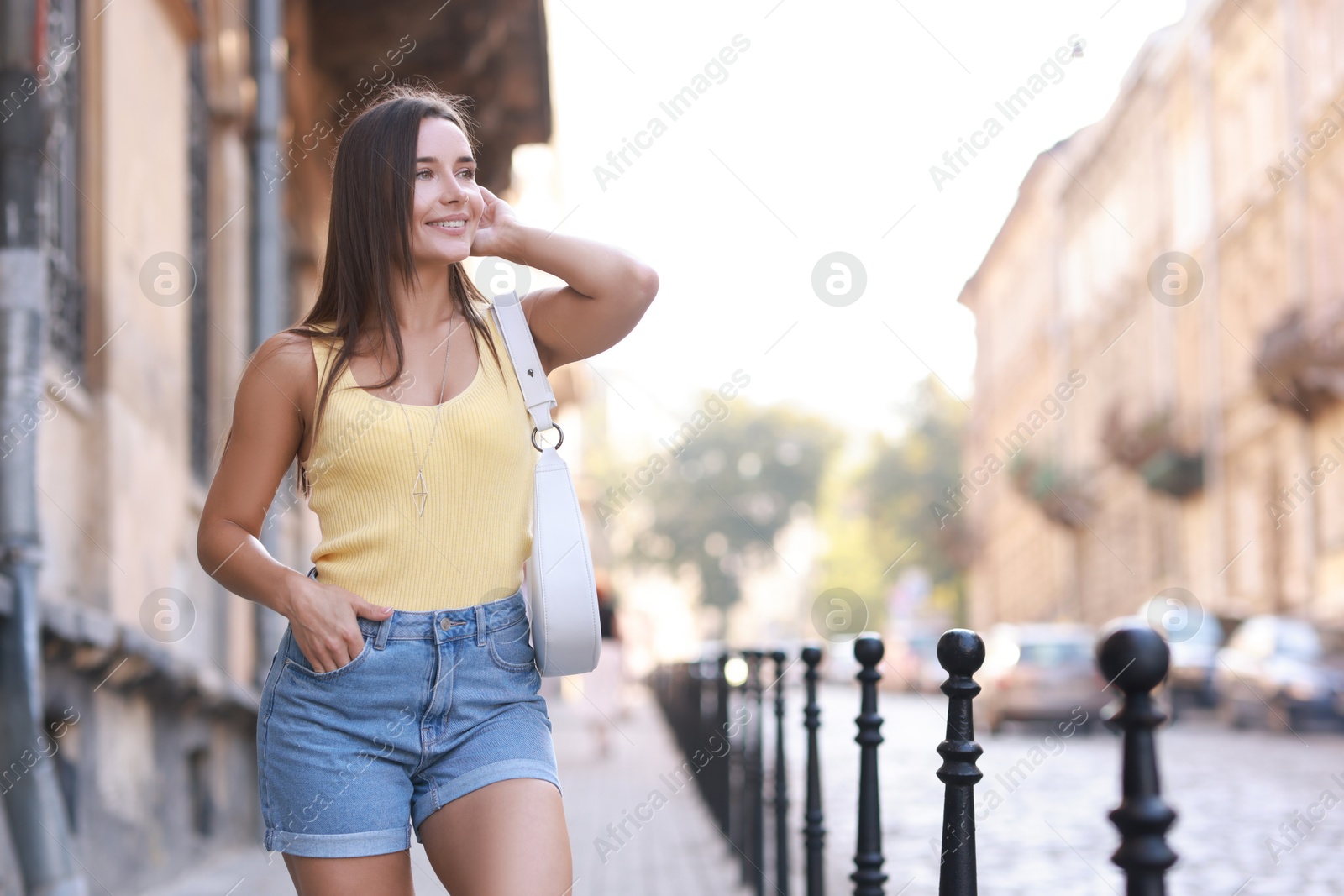 Photo of Beautiful woman with white bag wearing stylish denim shorts outdoors, space for text