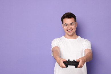 Happy young man playing video games with controller on violet background, space for text