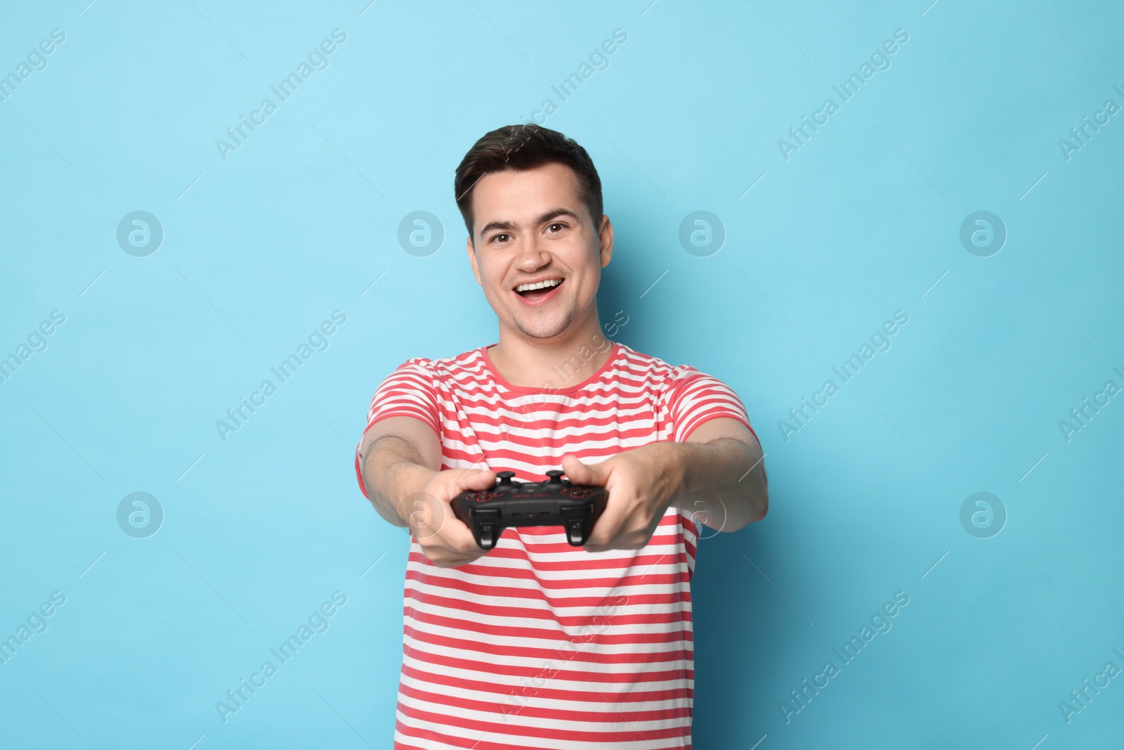 Photo of Happy young man playing video games with controller on light blue background