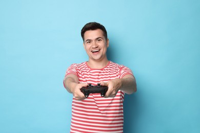 Happy young man playing video games with controller on light blue background