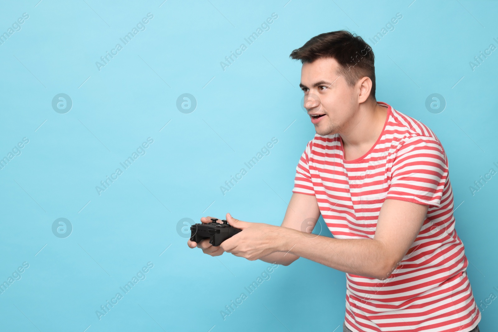 Photo of Happy young man playing video games with controller on light blue background, space for text