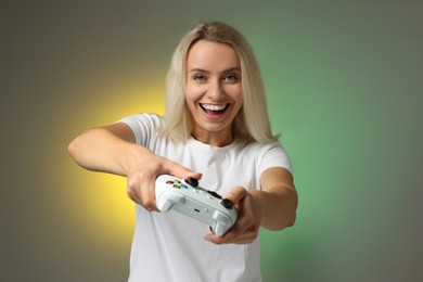 Happy woman playing video games with controller on color background