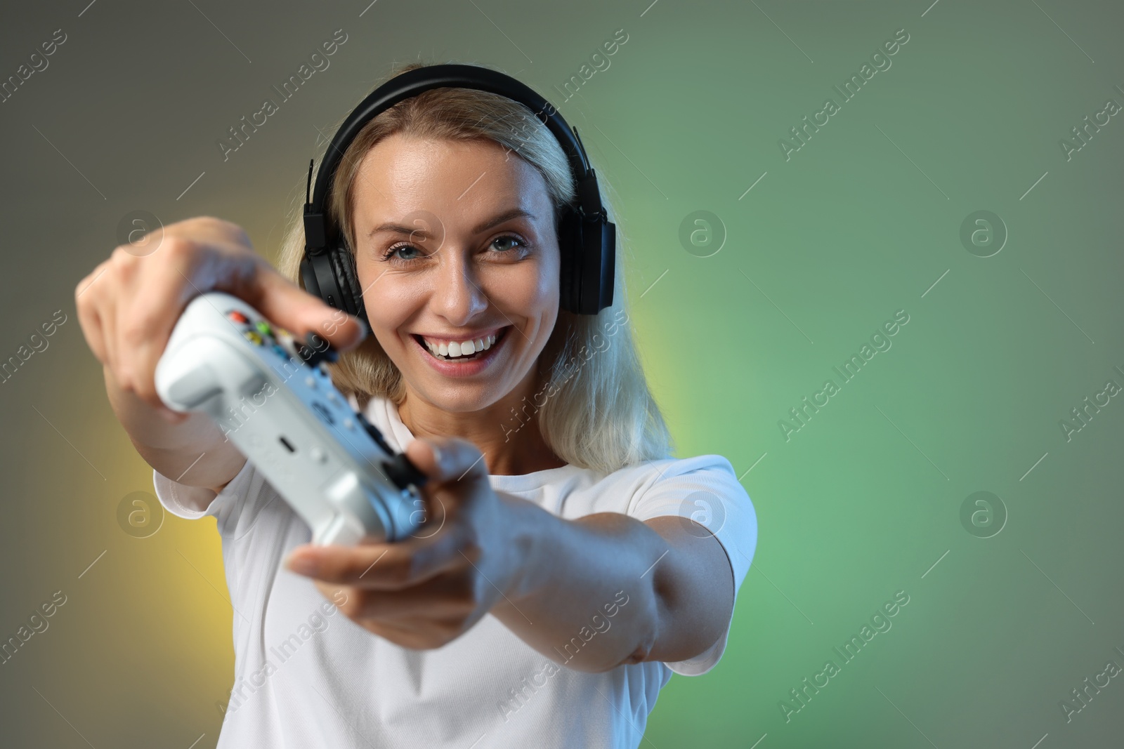 Photo of Happy woman in headphones playing video games with controller on color background, space for text