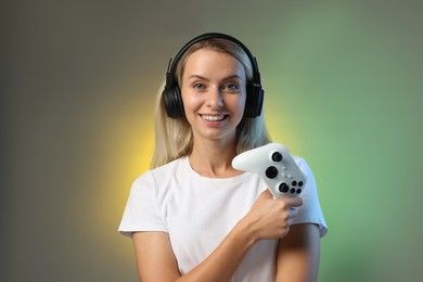 Happy woman in headphones with controller on color background