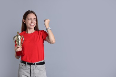 Photo of Happy winner with gold trophy cup on gray background, space for text