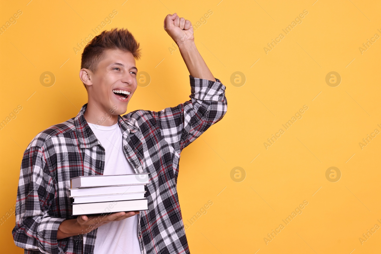 Photo of Young student with stack of books happy about his good exam result on yellow background, space for text