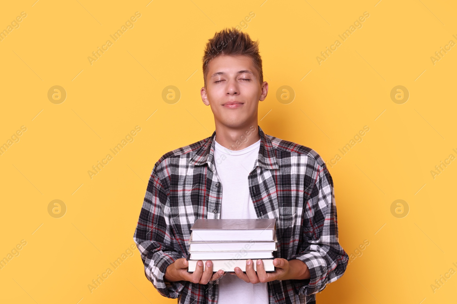 Photo of Young student with stack of books on yellow background