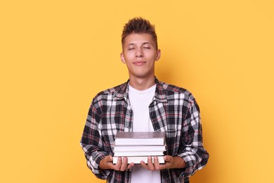 Photo of Young student with stack of books on yellow background