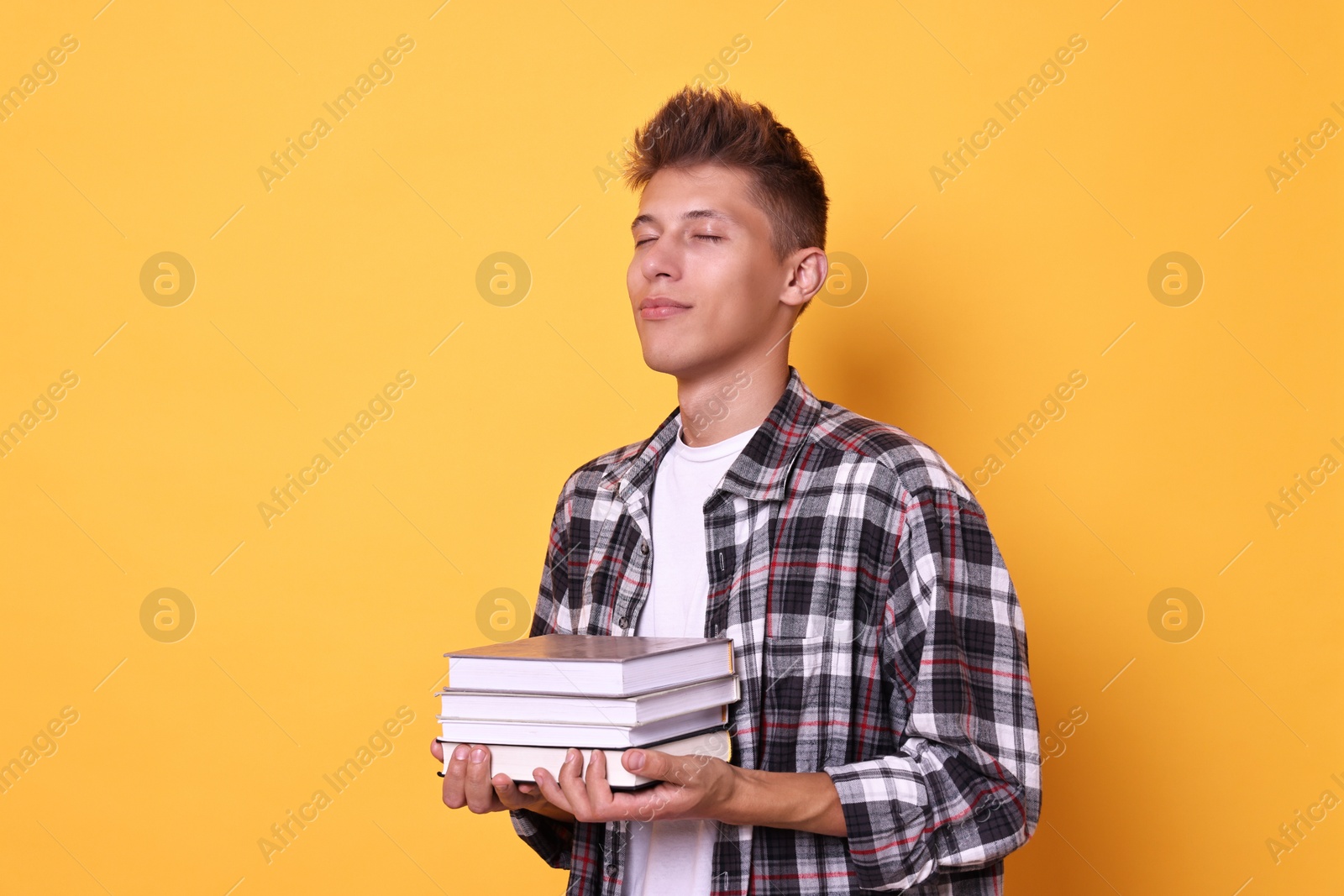 Photo of Young student with stack of books on yellow background