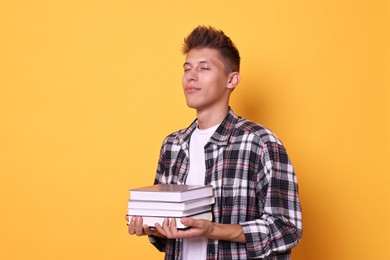 Young student with stack of books on yellow background