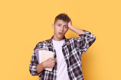 Young student with books having stress before exam on yellow background