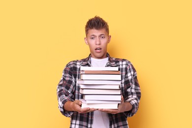 Young student with stack of books having stress before exam on yellow background