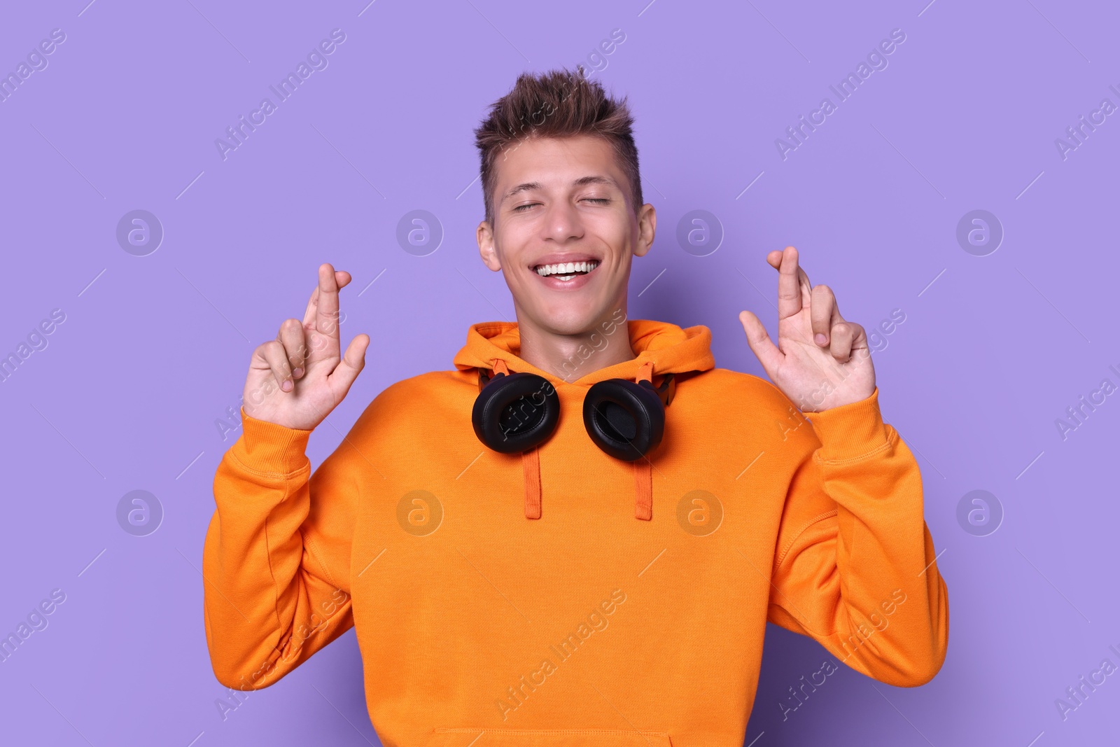 Photo of Excited young student crossing fingers on violet background. Hope for good exam result