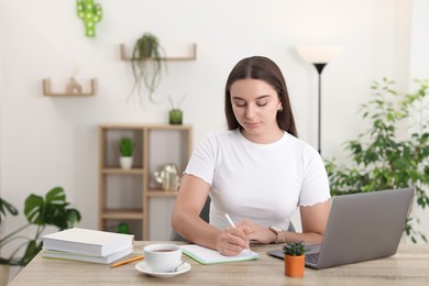 Student taking notes while studying at wooden table indoors