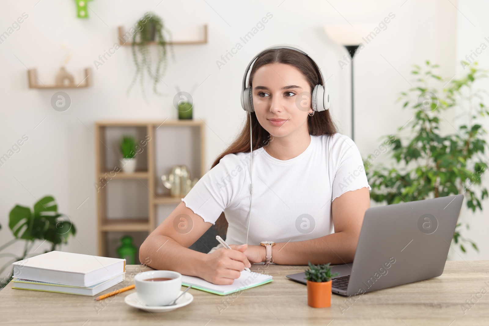 Photo of Student taking notes while studying at wooden table indoors