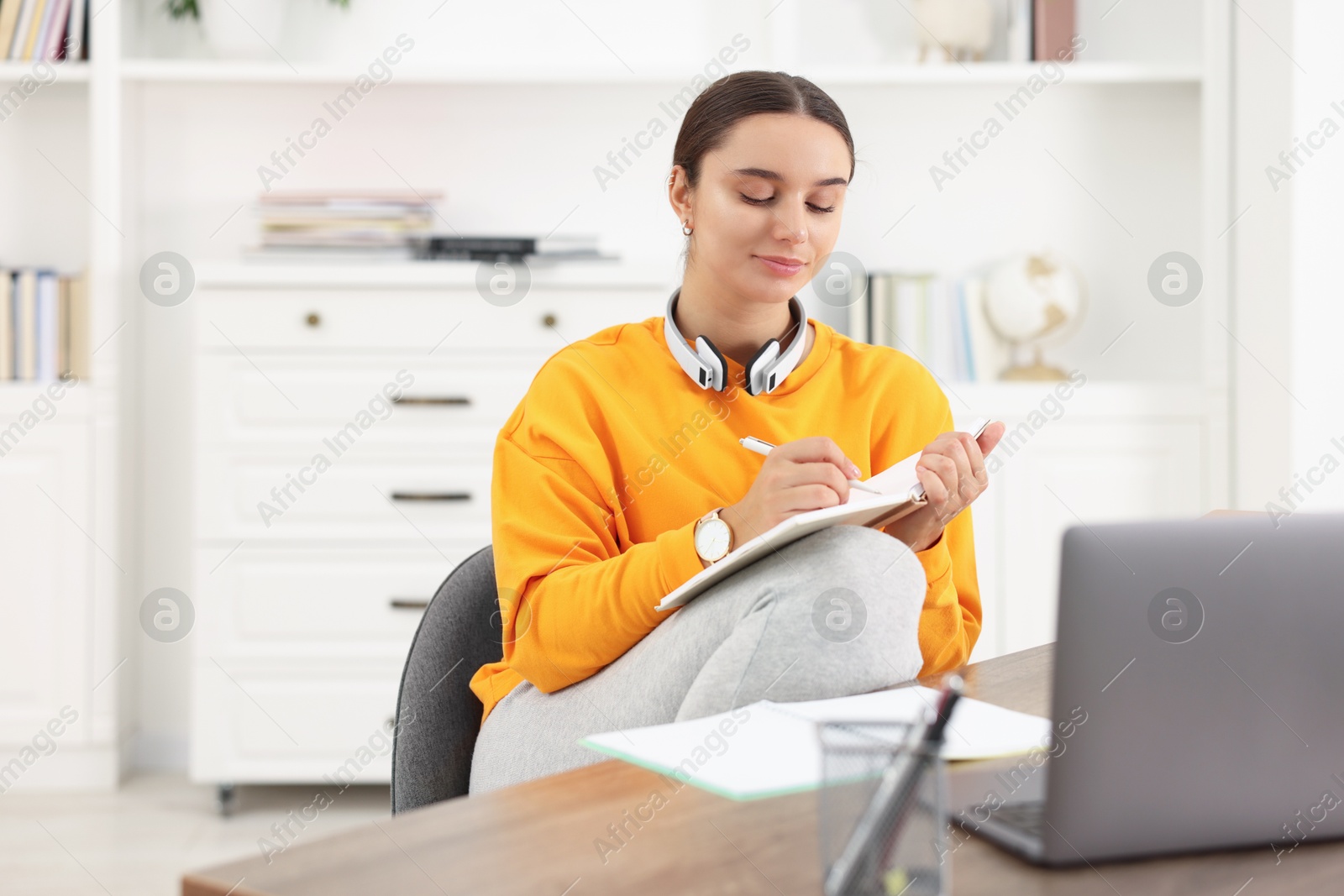 Photo of Student with headphones taking notes while studying indoors