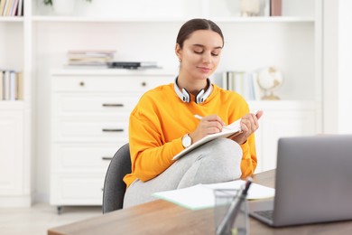 Student with headphones taking notes while studying indoors