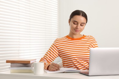 Student taking notes while studying at table indoors