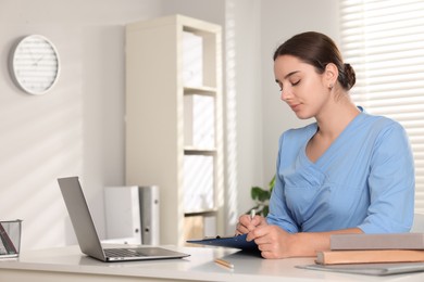 Medical student taking notes while studying at table indoors