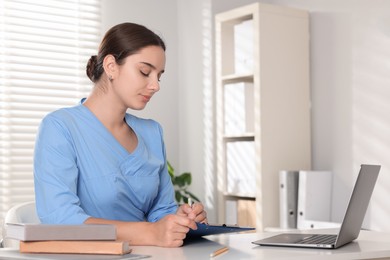 Photo of Medical student taking notes while studying at table indoors