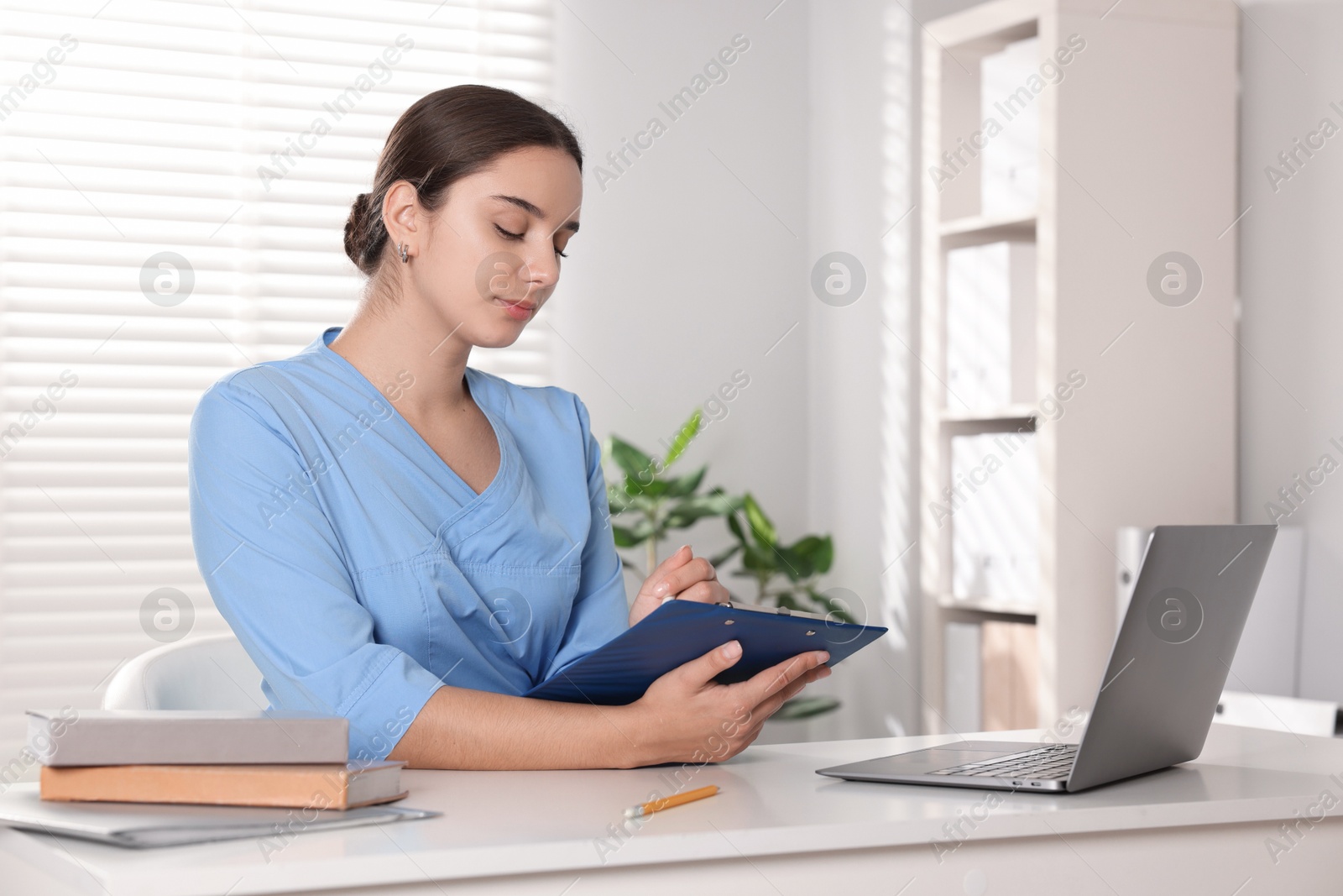 Photo of Medical student taking notes while studying at table indoors