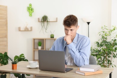 Student studying with laptop at wooden table indoors