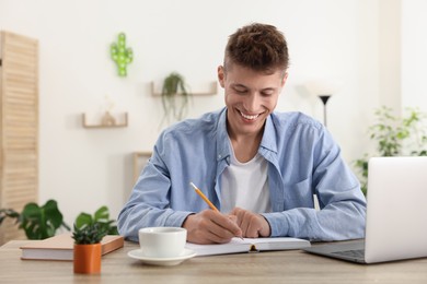 Photo of Student taking notes while studying at wooden table indoors