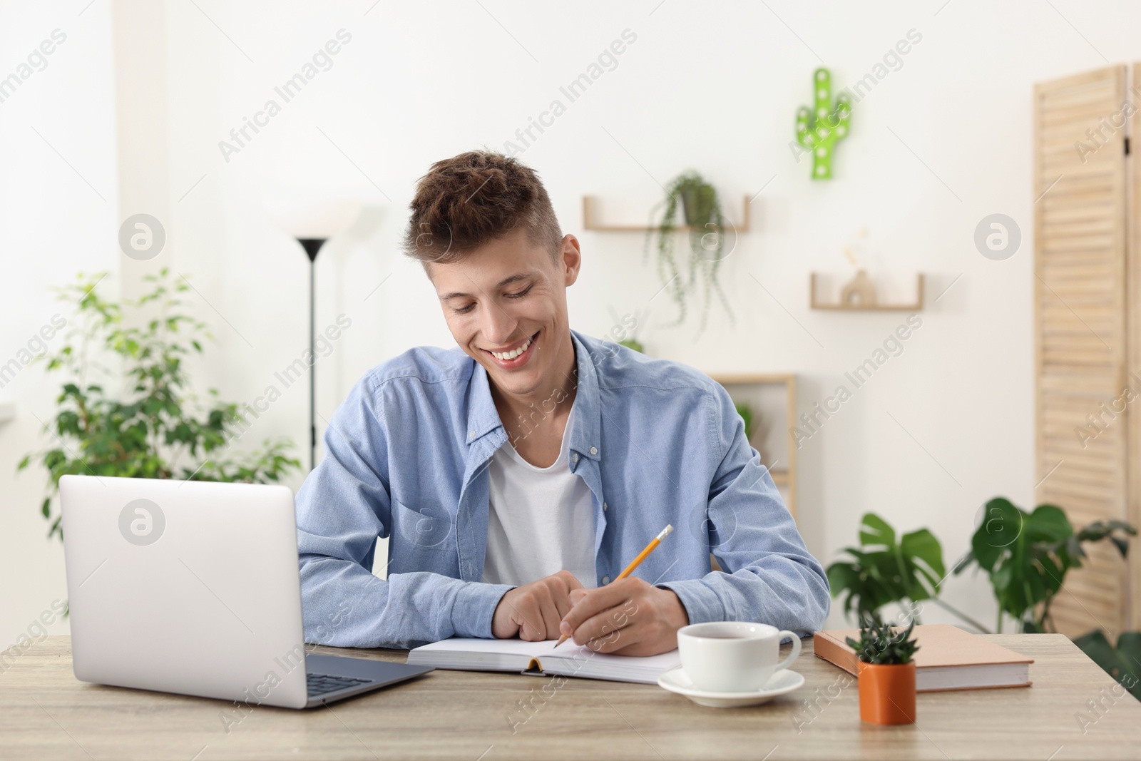 Photo of Student taking notes while studying at wooden table indoors