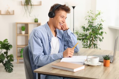 Photo of Student in headphones studying at wooden table indoors