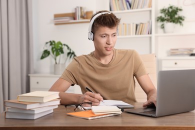 Student in headphones studying with laptop at table indoors