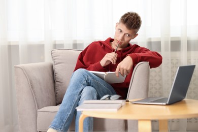 Student taking notes while studying in armchair at home