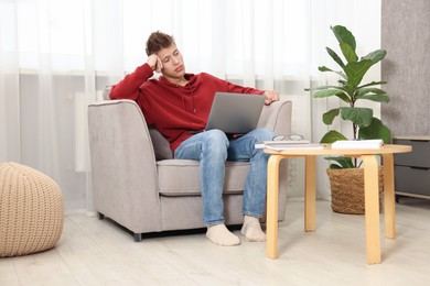 Student studying with laptop in armchair at home