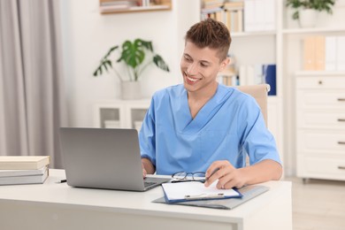 Medical student in uniform studying with laptop at table indoors