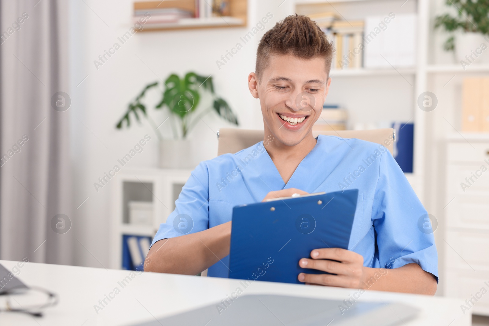 Photo of Medical student with clipboard studying at table indoors