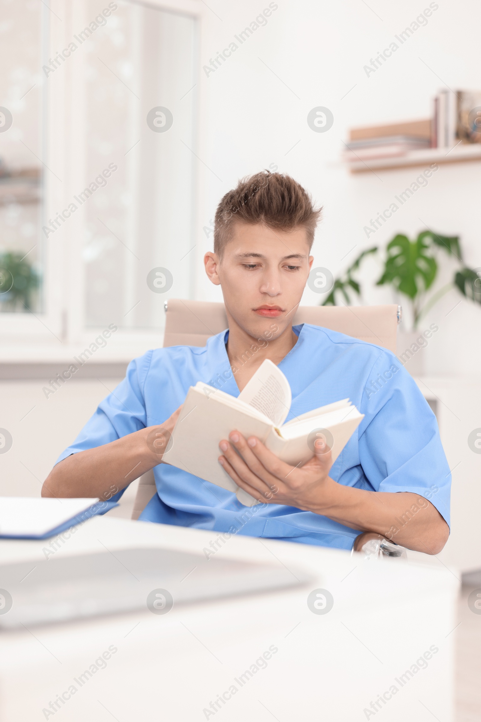 Photo of Medical student with book studying at table indoors